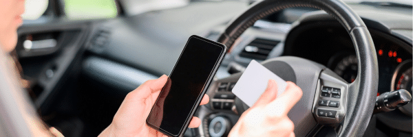 Person looking at phone and reading a card while driving | Picture used for Glasheen, Valles & Inderman Injury Lawyers | Houston Distracted Driving Accident Lawyer Page