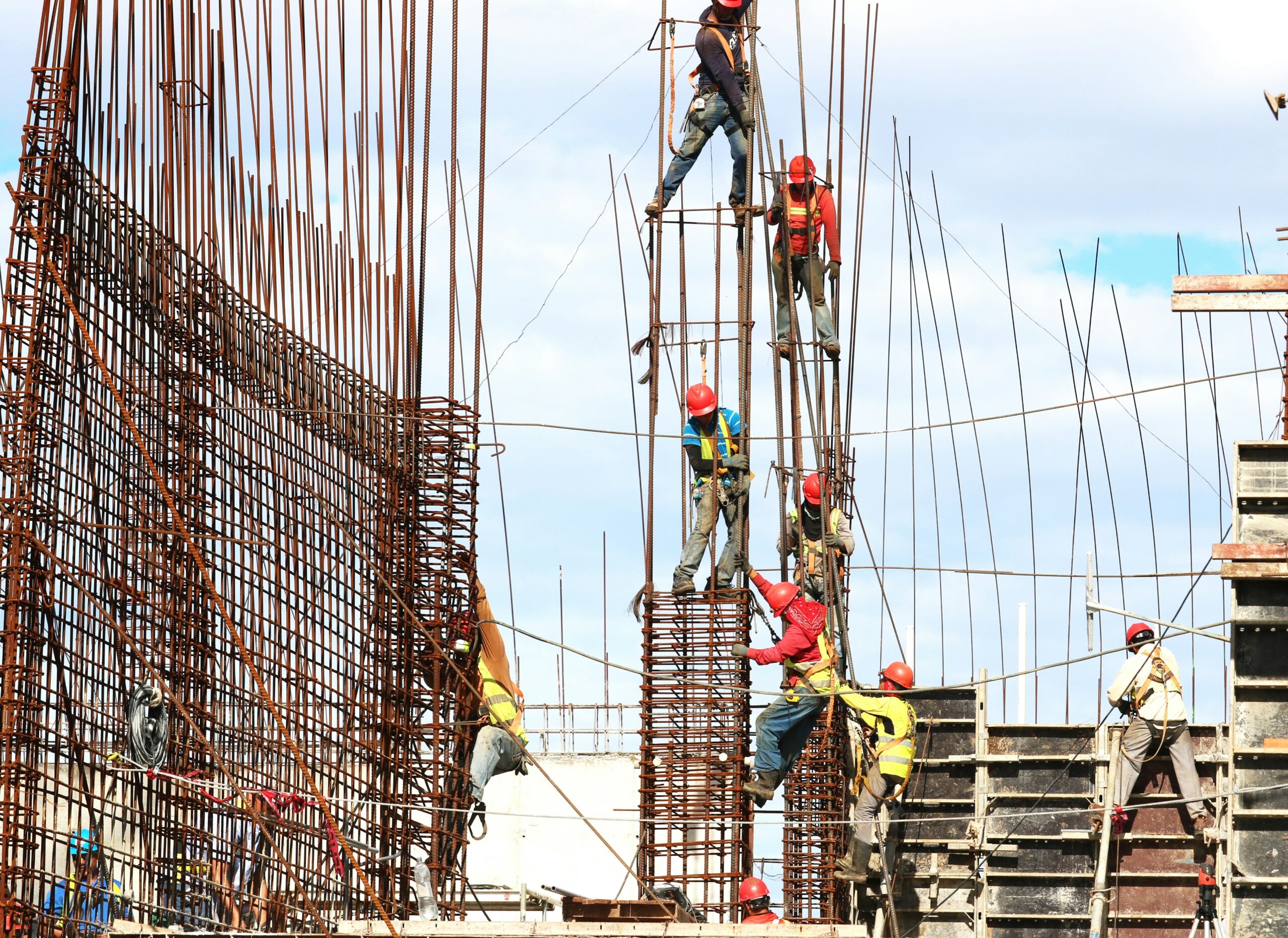 Picture showing workers in safety vests and hard hats climbing an unfinished structure to show an example of situations leading to Construction injury